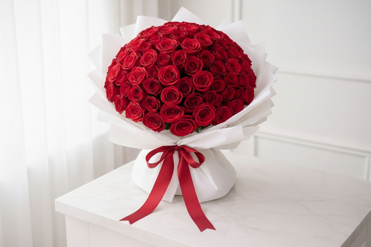 Bouquet of red roses wrapped in white paper with a bow on a white surface.