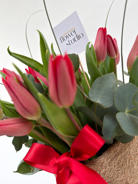 Bouquet of red tulips with a red ribbon and 'Northumberland Flower Studio' tag on a white background