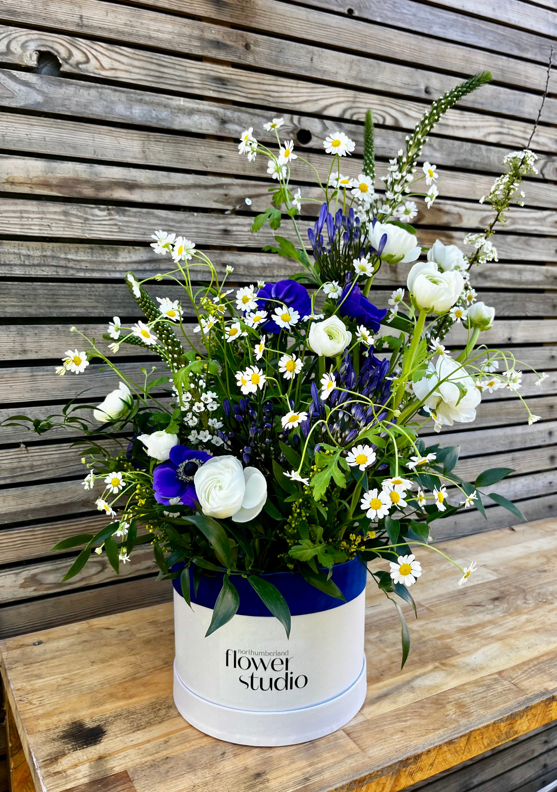 Floral arrangement in a white hat box with 'Northumberland flower studio' branding on a wooden surface.