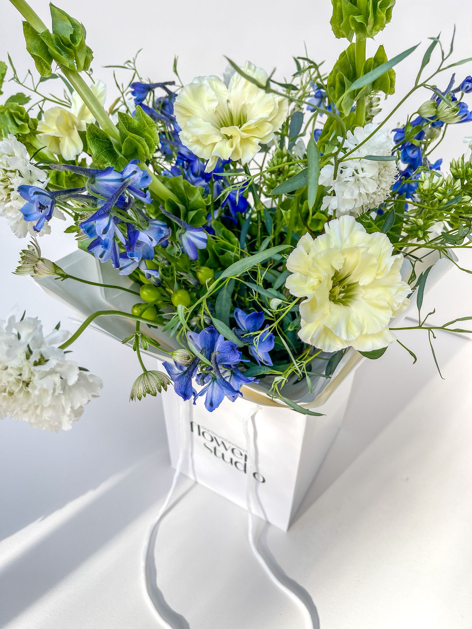 Bouquet of blue and white flowers in a white box with 'Flower Studio' branding on a light background