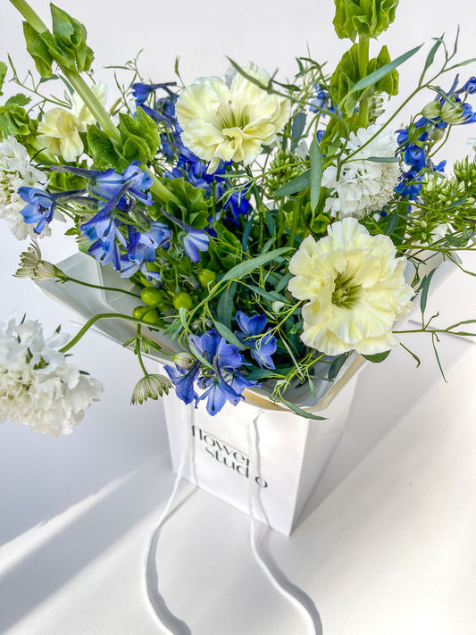 Bouquet of blue and white flowers in a white box with 'Flower Studio' branding on a light background
