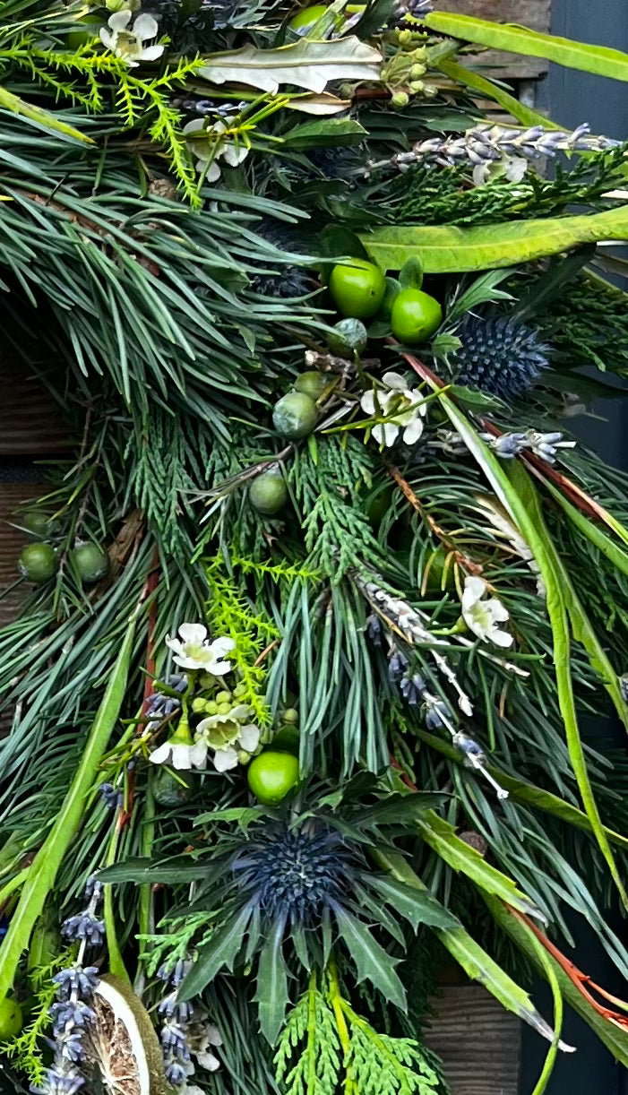 Close-up of a festive wreath with greenery, berries, and flowers on a wooden surface.