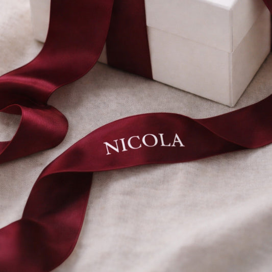 White gift box with a red ribbon featuring the name 'NICOLA' on a beige surface.
