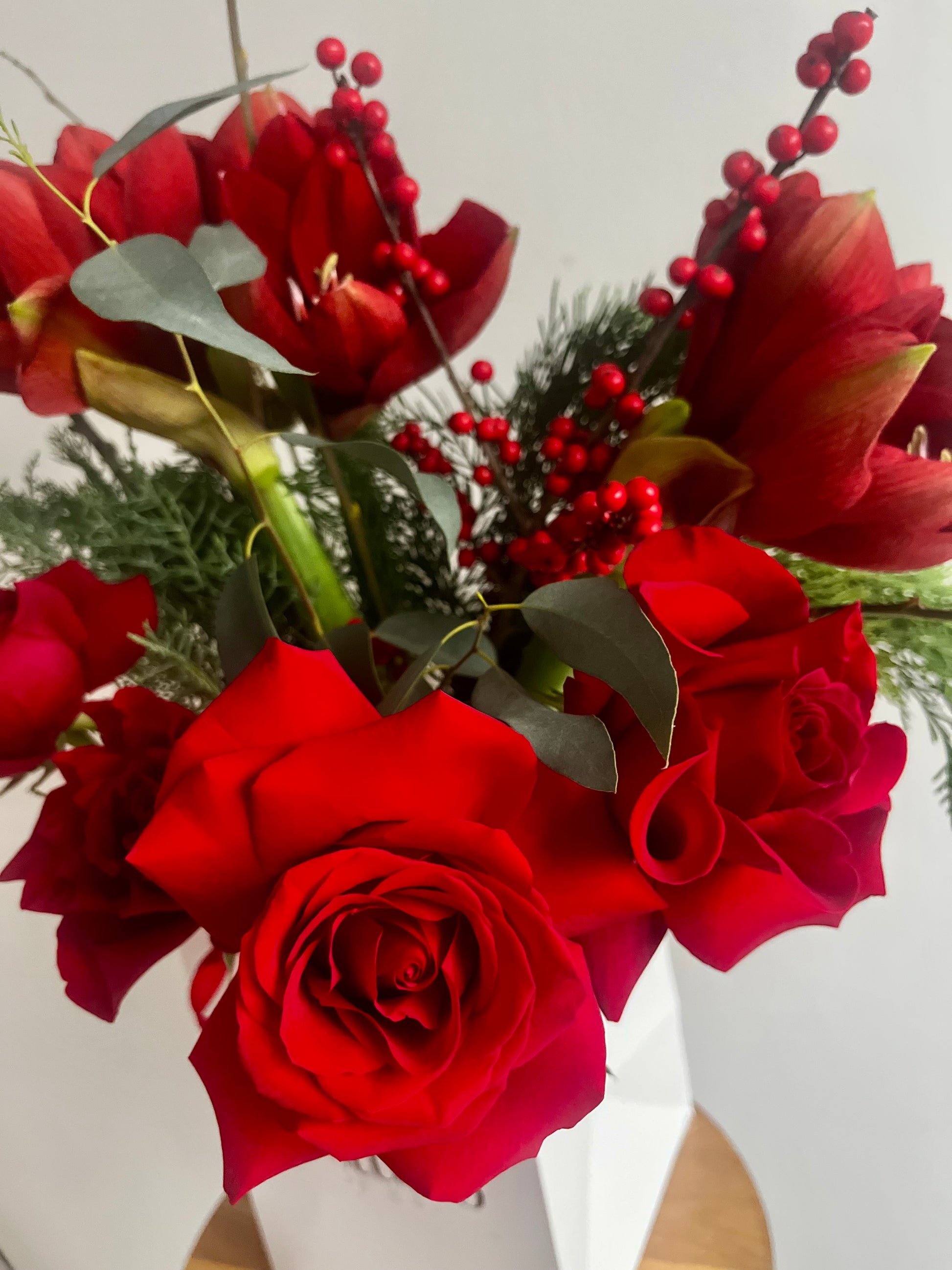 Bouquet of red roses and Amarylis with green leaves and red berries in a white gift bag