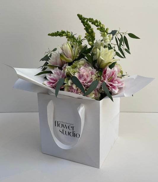 Hand-tied floral arrangement in a white gift bag with 'Northumberland Flower Studio' branding on a light background