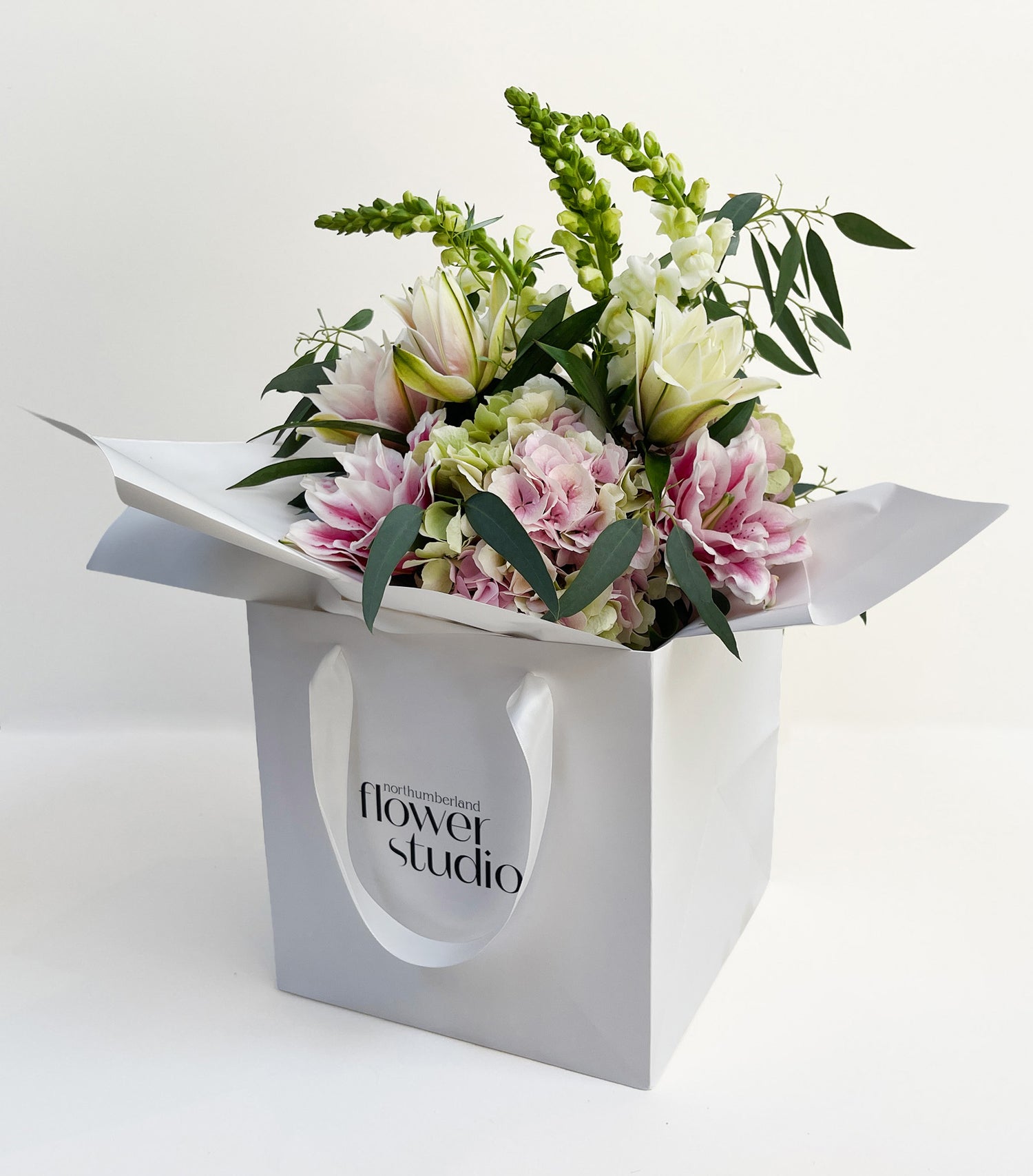 Hand-tied floral arrangement in a white gift bag with 'Northumberland Flower Studio' branding on a light background