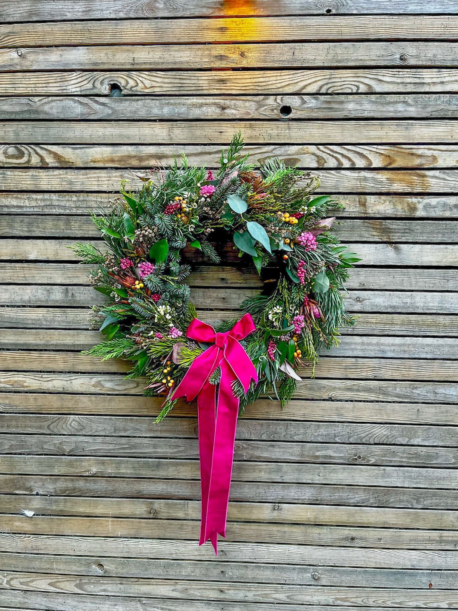Christmas wreath with a pink ribbon on a wooden wall