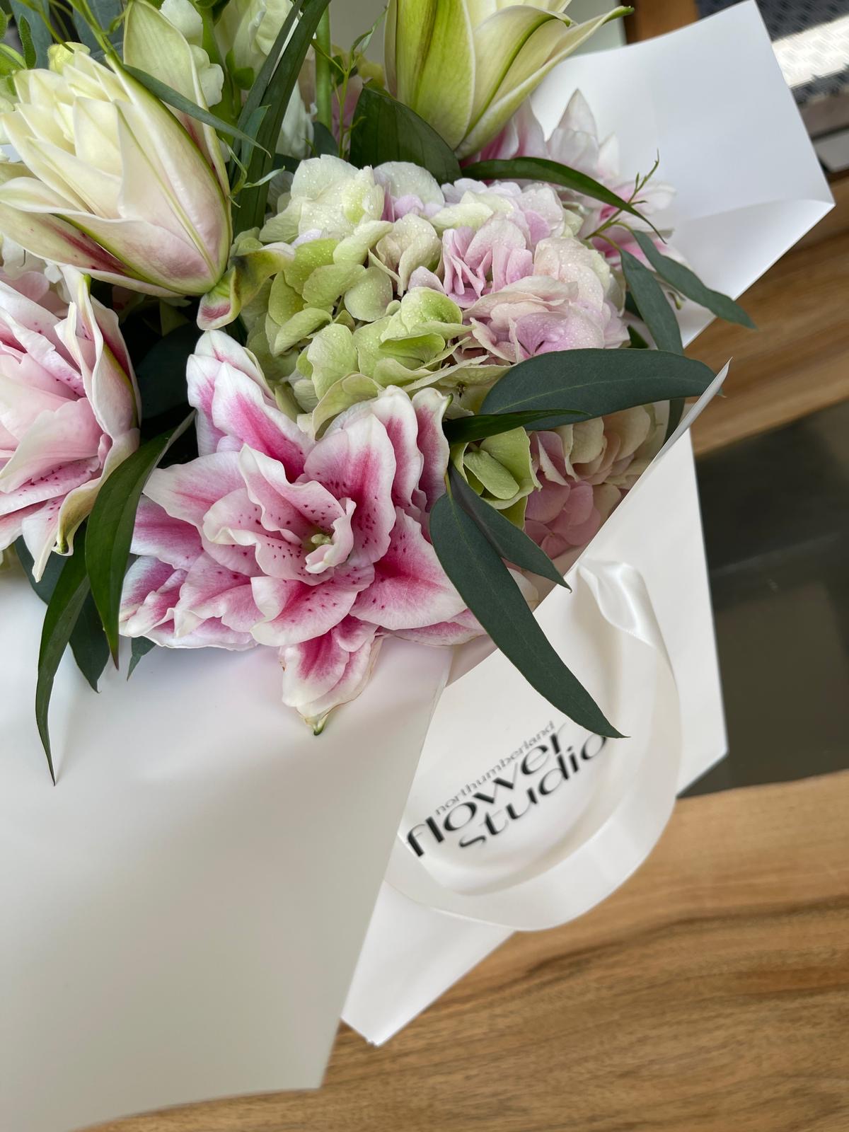 Bouquet of flowers wrapped in white paper with 'Northumberland Flower Studio' branding on a wooden surface