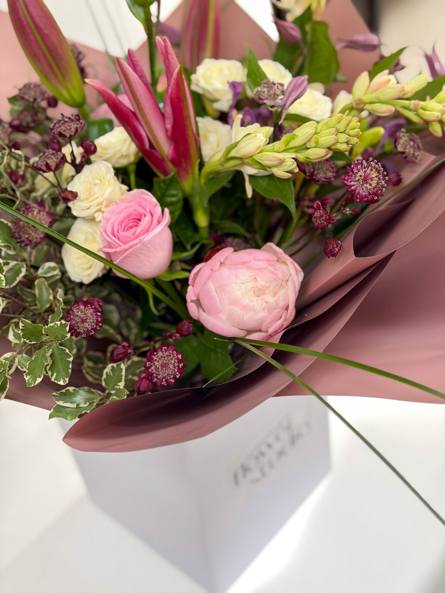 Bouquet of peonies wrapped in pink paper on a white surface