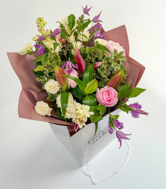 Bouquet of flowers wrapped in pink paper with a white box on a light background