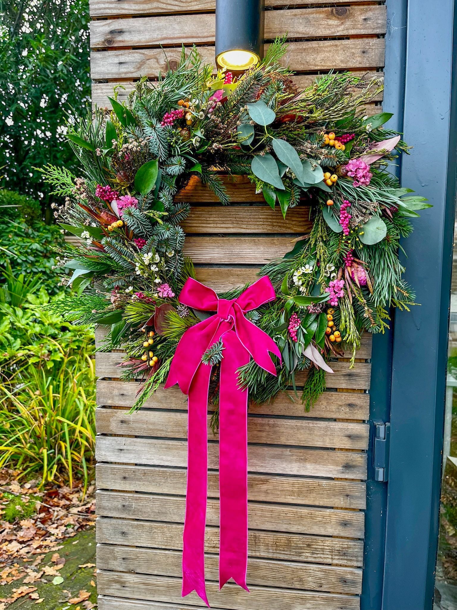Decorative Christmas wreath with a pink ribbon on a wooden door outdoors