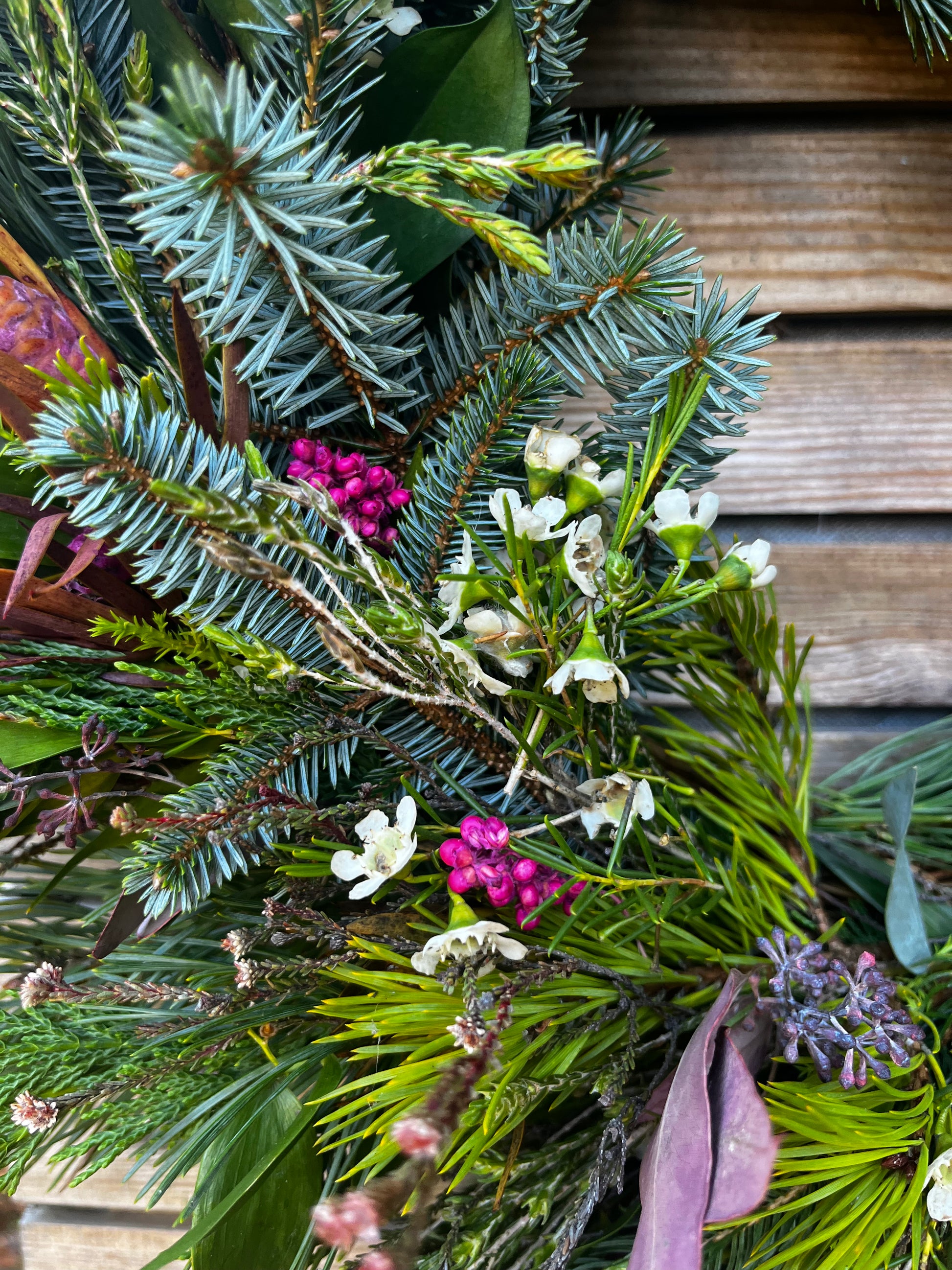Close-up of a festive wreath with greenery, berries, and flowers against a wooden background