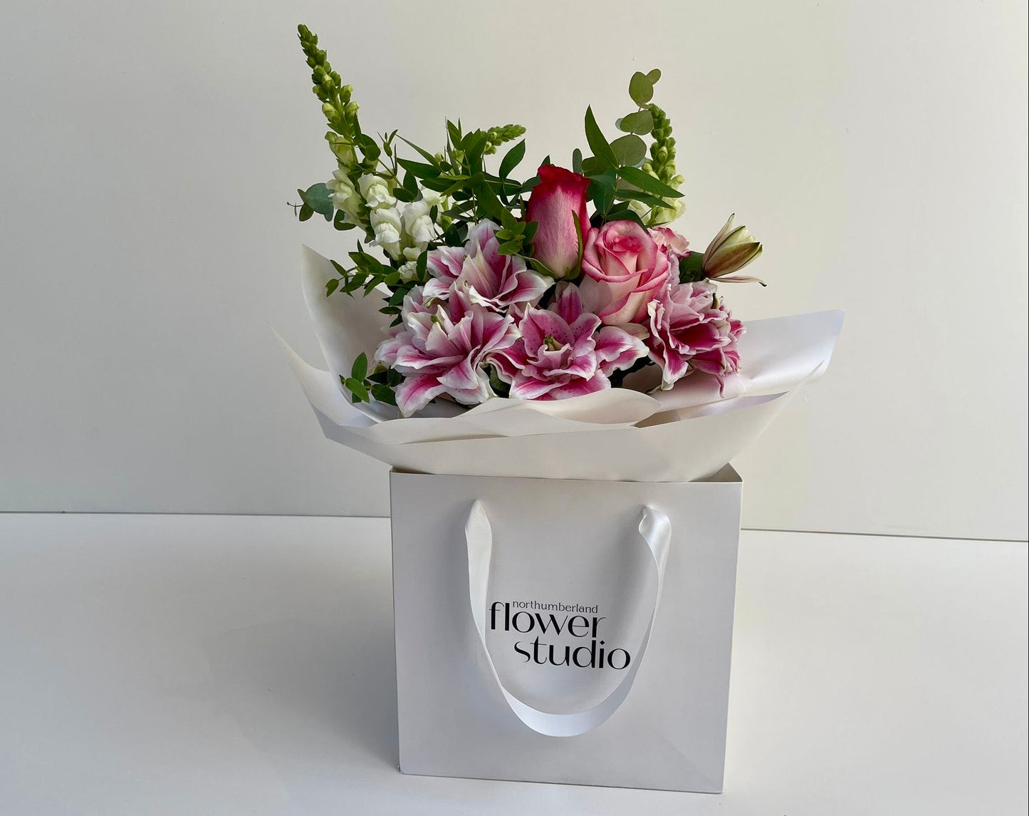 Bouquet of flowers in a white wrap with 'flower studio' branding on a white background