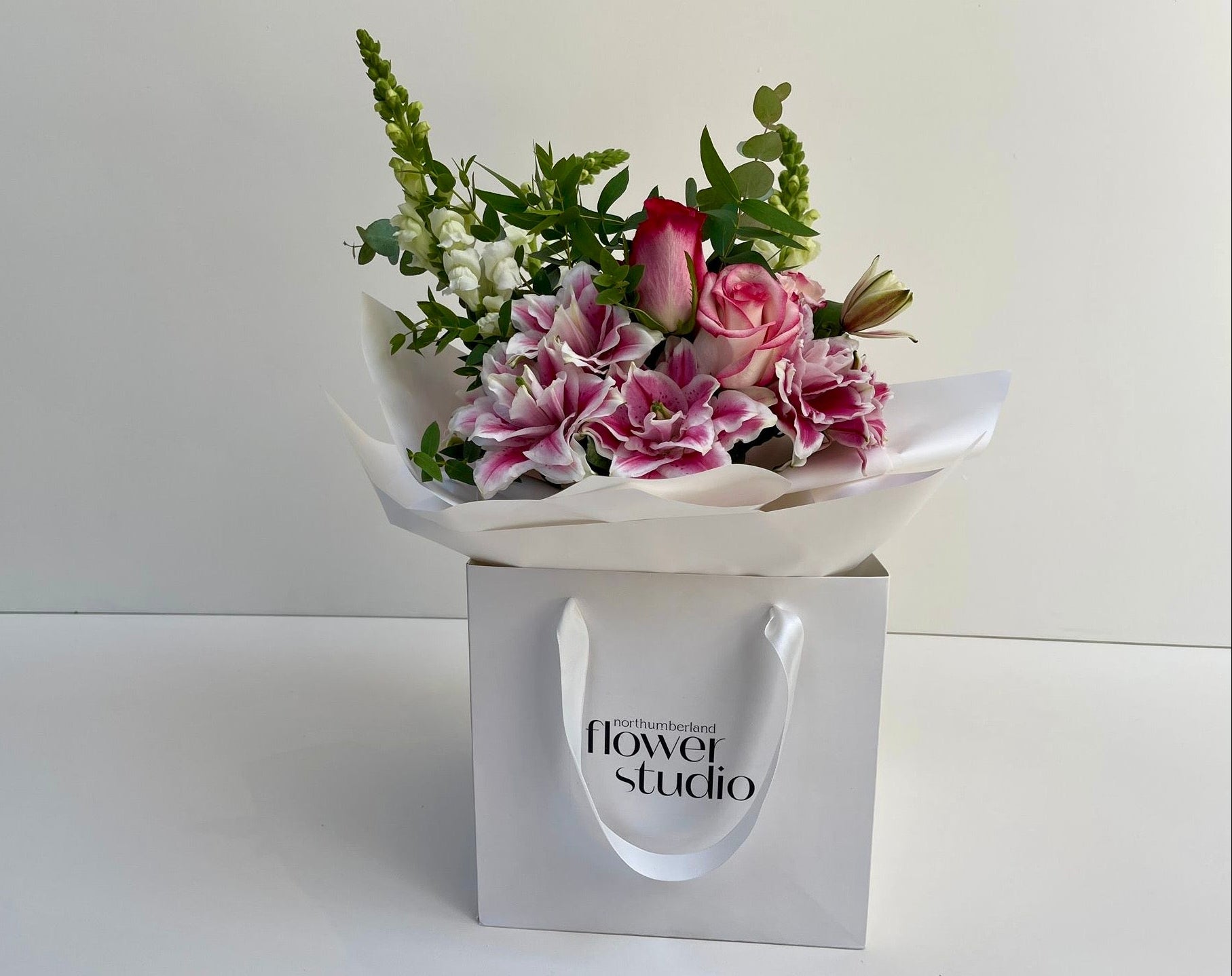 Bouquet of flowers in a white wrap with 'flower studio' branding on a white background