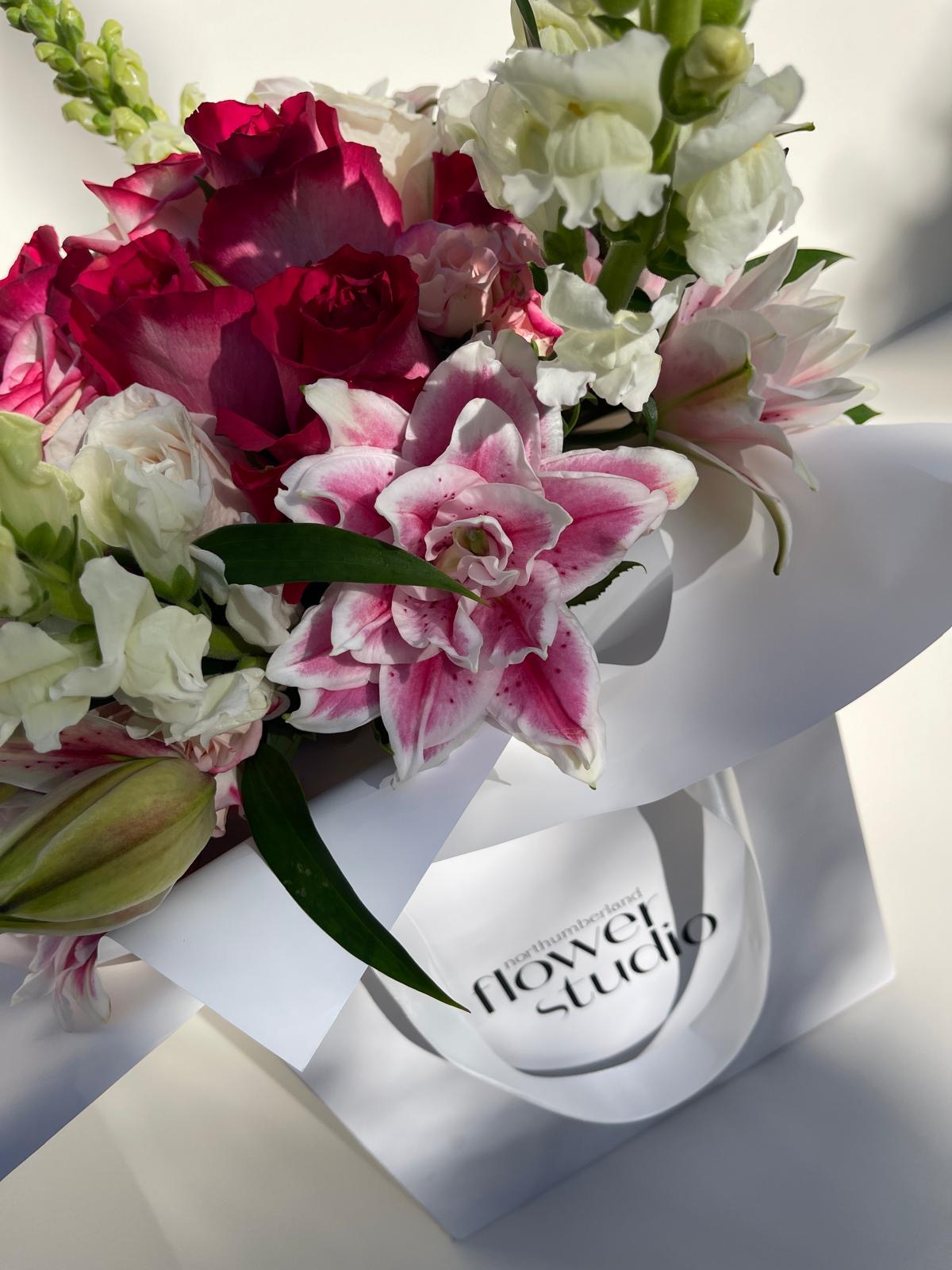 Bouquet of flowers in a white gift bag with 'Northumberland Flower Studio' branding on a light background